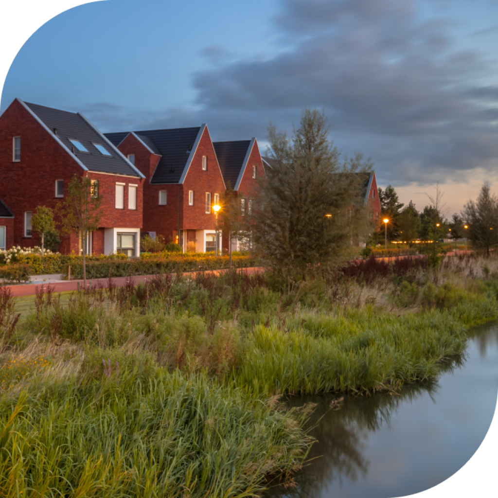 A row of suburban houses in a row next to the lake at night time. The street lamps are on and there is a strip of green between the new builds and the lake.